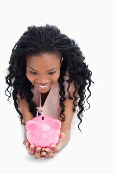 Uma mulher sorrindo está olhando para um banco porquinho que ela está segurando — Fotografia de Stock