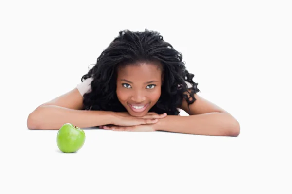 Una chica sonriente está apoyando su cabeza en sus manos con una manzana en — Foto de Stock