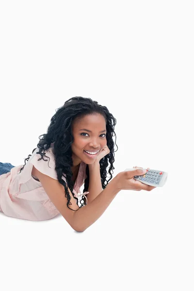 A young girl holding a television remote control is smiling at t — Stock Photo, Image
