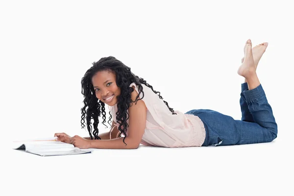 Een vrouw die liggend op de vloer glimlachen op de camera met een magazine — Stockfoto
