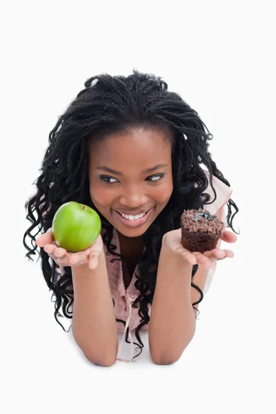 Een lachende jonge vrouw houdt een appel en een broodje op de handpalmen — Stockfoto
