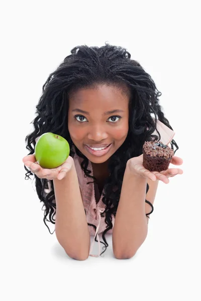 A young woman looking at the camera is holding an apple and a bu — Stock Photo, Image