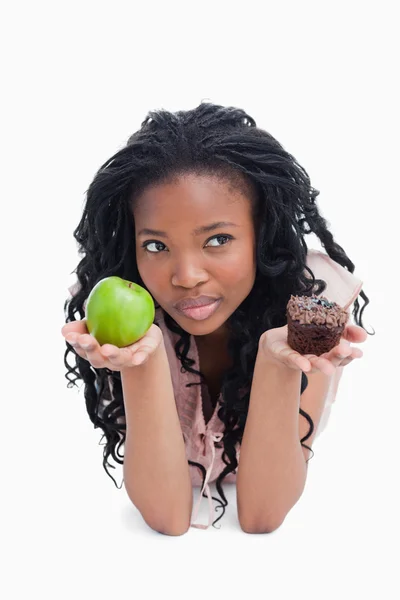 A woman holding an apple and a bun on her palms is thinking — Stock Photo, Image