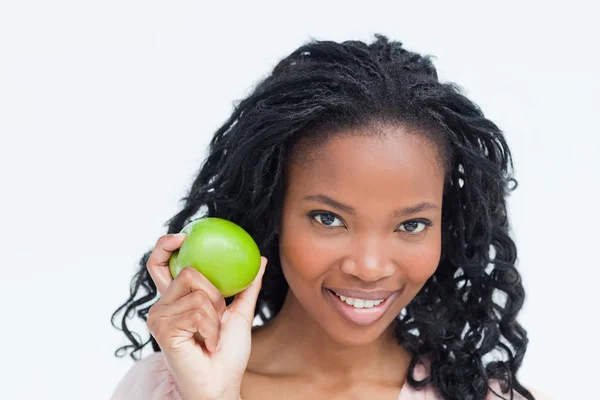 Una joven sonriente sosteniendo una manzana junto a su cara — Foto de Stock