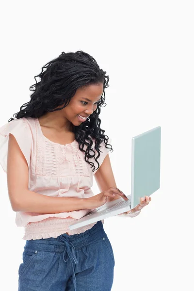 Eine glückliche junge Frau tippt auf dem Laptop, den sie in der Hand hält — Stockfoto