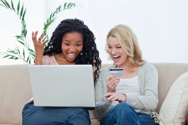 Dos mujeres riendo con un portátil y una tarjeta bancaria —  Fotos de Stock