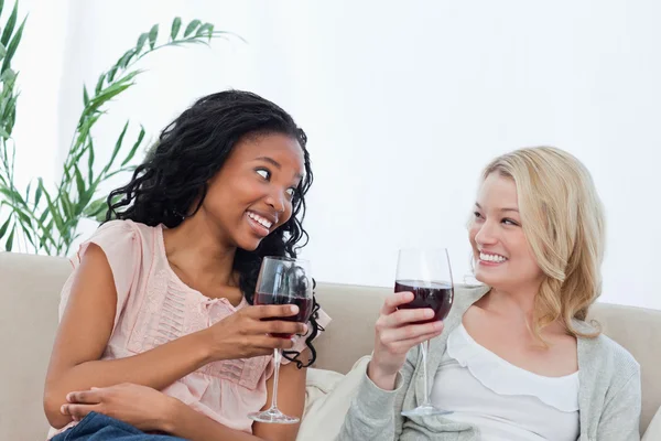 坐在沙发上的两名妇女正在举行葡萄酒杯 — 图库照片