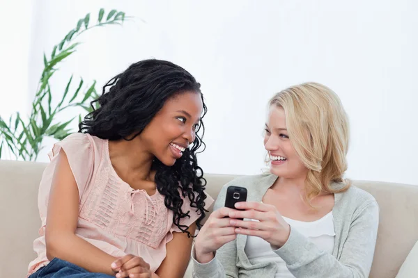 Uma mulher segurando um telefone celular está sorrindo para sua amiga — Fotografia de Stock