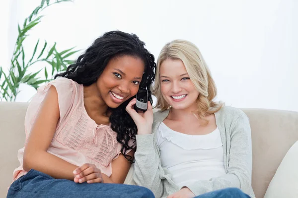 Dos mujeres escuchando un teléfono móvil sonríen a la cámara — Foto de Stock