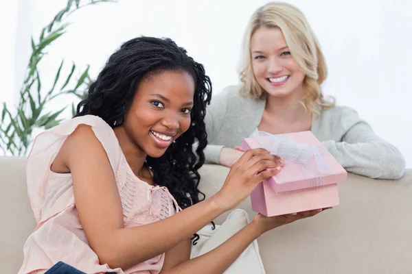 A nő, kezében egy rózsaszín doboz mosolyog a kamera, a barátja — Stock Fotó