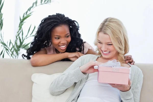 Una mujer sonriente sostiene una caja rosa y su amiga está detrás de h — Foto de Stock