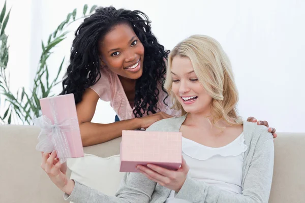 Una mujer abre una caja que contiene un regalo y su amiga sonríe —  Fotos de Stock