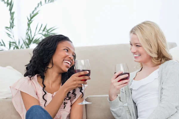 Две женщины сидят на полу и говорят и пьют вино. — стоковое фото