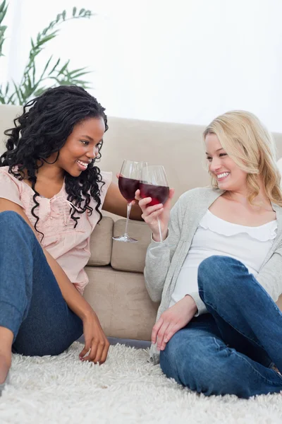 Dos mujeres están sentadas en el suelo hablando y sosteniendo vino gla —  Fotos de Stock
