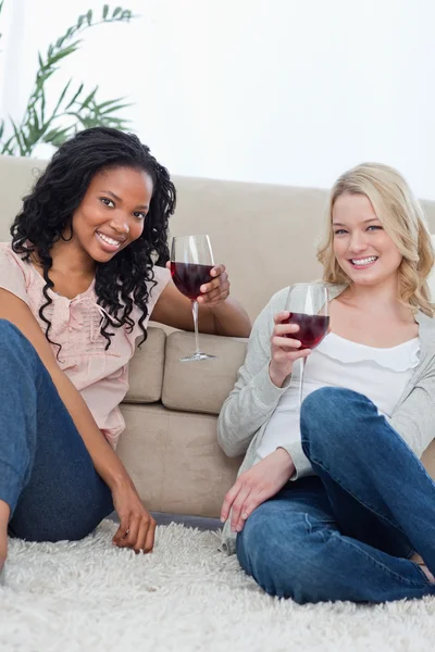 Zwei Frauen, die mit Weingläsern in die Kamera lächeln — Stockfoto