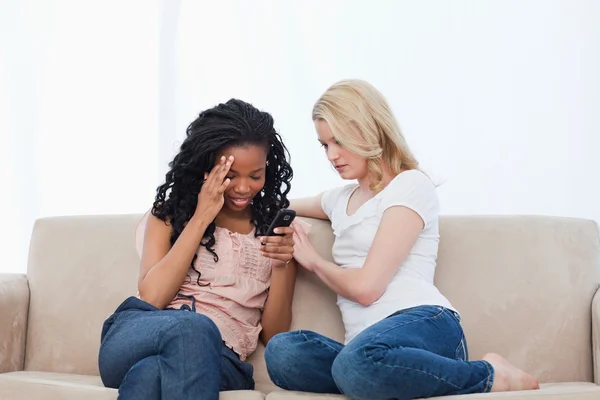 Две женщины, сидящие на диване, смотрят на мобильный телефон — стоковое фото