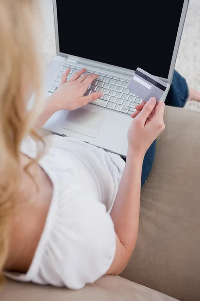 Overhead view of a woman holding a bank card and typing on a lap — Stock Photo, Image