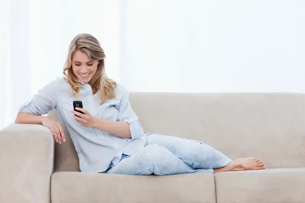Žena sedící na gauči drží mobilní telefon — Stock fotografie
