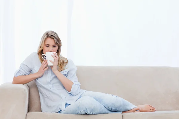 Bir fincan kahve içme bir kadın kanepede yatıyor — Stok fotoğraf