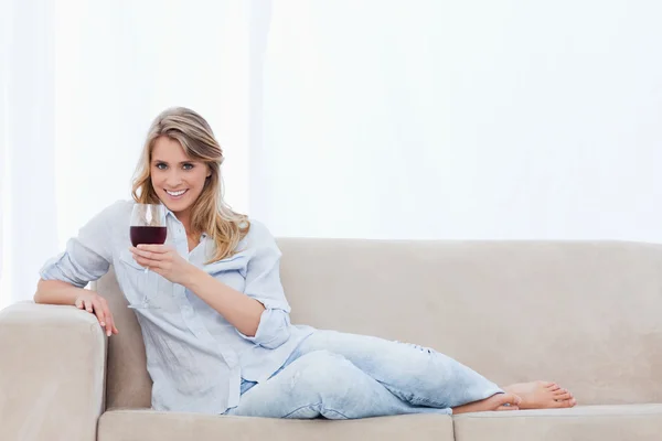 Kanepede yatan bir gülümseyen kadın şarap tutuyor — Stok fotoğraf