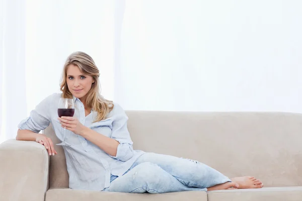 Uma mulher olhando para a câmera está segurando um copo de vinho tinto — Fotografia de Stock
