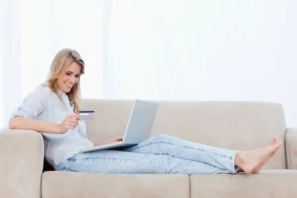 Женщина, лежащая на диване с ноутбуком перед ней, держит — стоковое фото