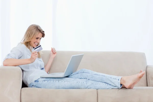 En glad kvinna med ett bankkort har en bärbar dator på benen — Stockfoto