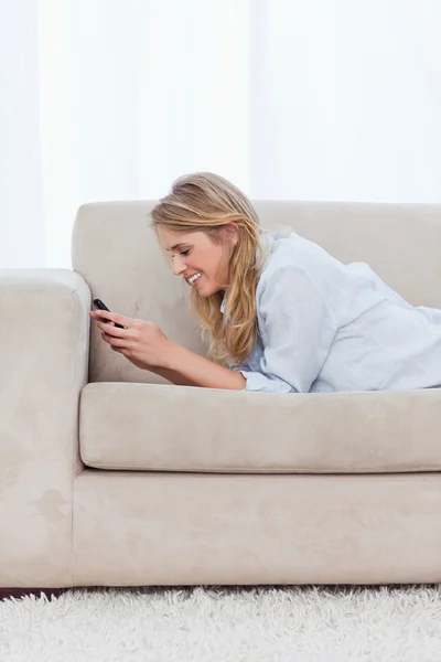 Una mujer que descansa sobre sus codos está enviando mensajes de texto en su teléfono móvil —  Fotos de Stock