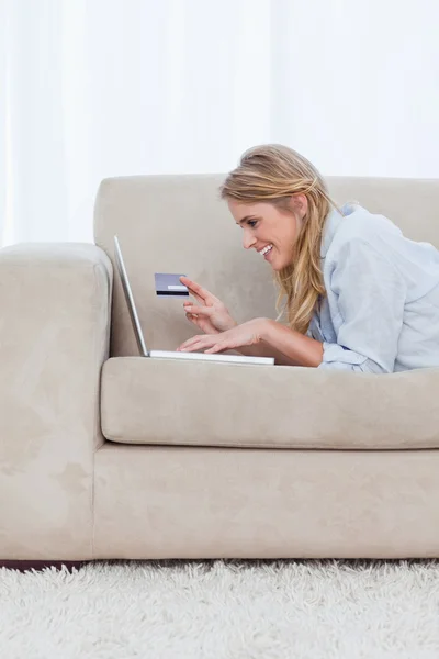 Een vrouw op haar ellebogen rustend is een bankkaart te houden en te typen — Stockfoto