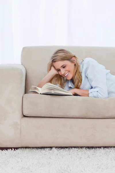 A smiling woman lying on a couch resting her head on her hand is — Stock Photo, Image