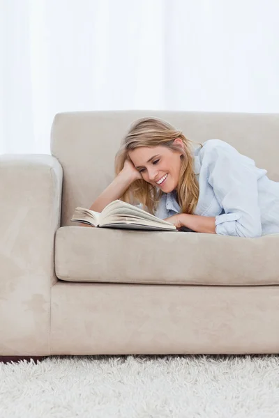 Een lachende vrouw liggend op een bank rustend haar hoofd op haar hand is — Stockfoto