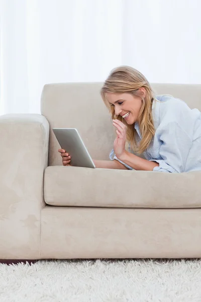 여자는 태블릿을 들고 소파에 누워 웃 — 스톡 사진