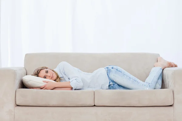 Eine Frau liegt auf einer Couch und legt ihren Kopf auf ein Kopfkissen — Stockfoto
