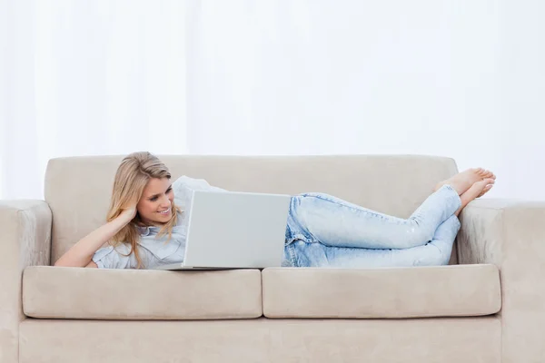 Una donna sdraiata su un divano appoggiando la testa sulla mano sta usando h — Foto Stock