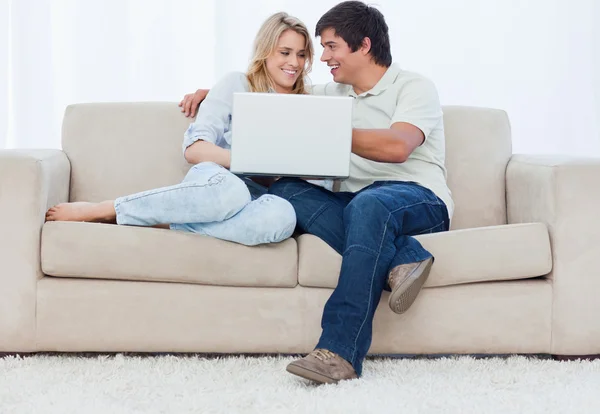 Een jong koppel zittend op een bank met een laptop — Stockfoto