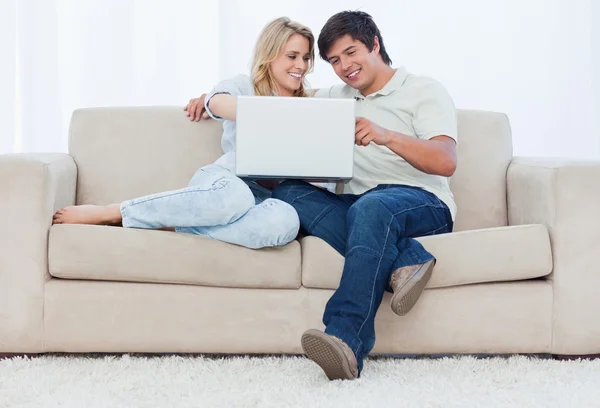 Um casal sorrindo está sentado em um sofá olhando para um laptop — Fotografia de Stock
