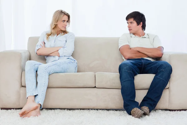 Um casal se senta nas duas extremidades do sofá com os braços dobrados — Fotografia de Stock