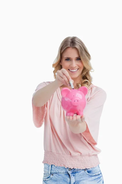 Lachende vrouw geld steken in een piggy bank die zij houdt — Stockfoto