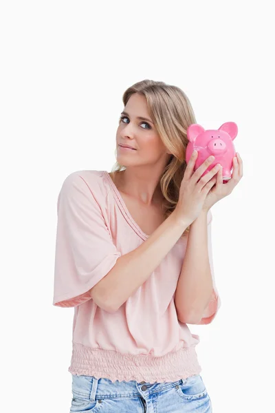 Woman holding a piggy bank up to her head — Stock Photo, Image