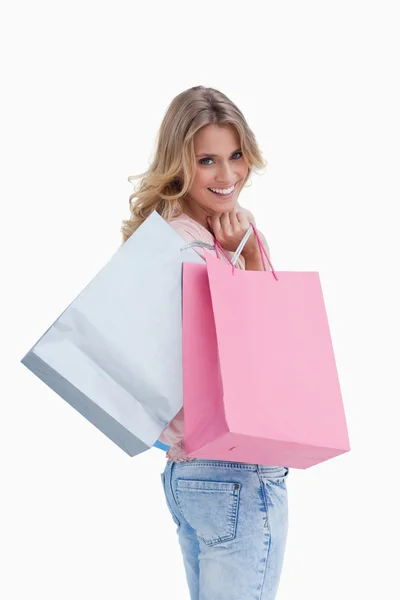 A woman looking back at the camera is carrying shopping bags ove — Stock Photo, Image