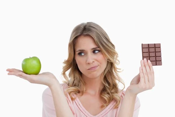 Jonge blonde vrouw aarzelen tussen chocolade en een apple — Stockfoto