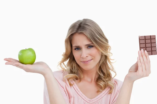 Young blonde woman holding an apple and a chocolate bar — Stock Photo, Image