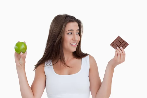 Young brunette woman holding a piece of chocolate and an apple — Stock Photo, Image