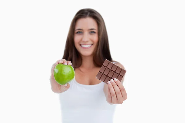A green apple and a piece of chocolate being held by a woman — Stock Photo, Image