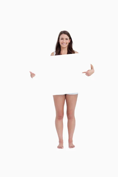 Mulher sorridente apontando um cartaz em branco — Fotografia de Stock