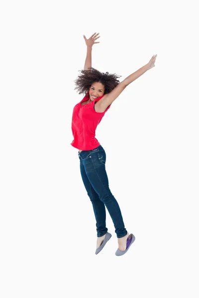 Sorrindo jovem morena pulando enquanto levanta os braços acima dela — Fotografia de Stock