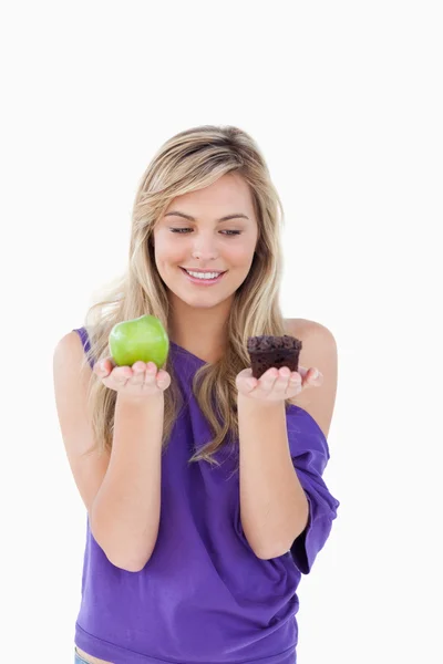 Усміхнена блондинка тримає яблуко і кекс — стокове фото