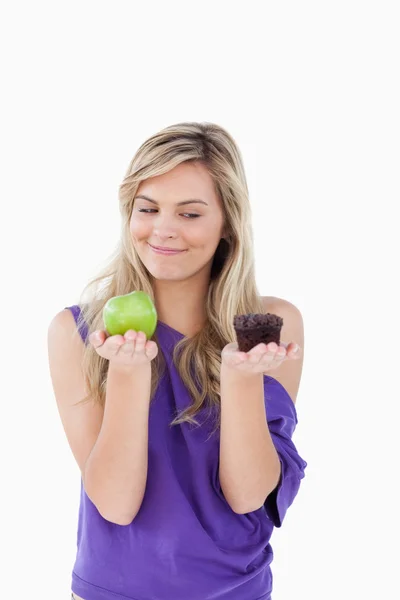 Thoughtful blonde woman holding an apple and a muffin — Stock Photo, Image