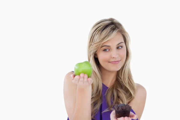 Peaceful blonde woman holding a green apple and a muffin — Stock Photo, Image
