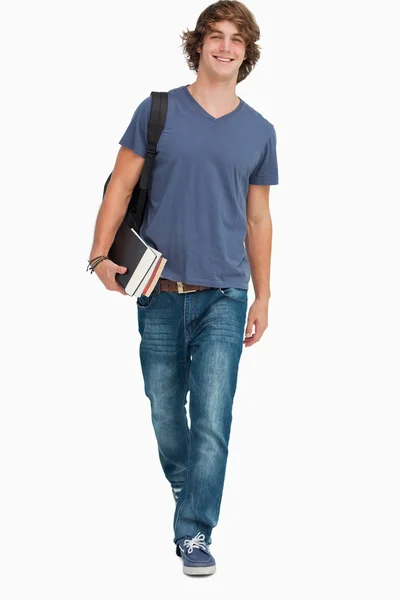 Vista frontal de um estudante caminhando com uma mochila e livros — Fotografia de Stock